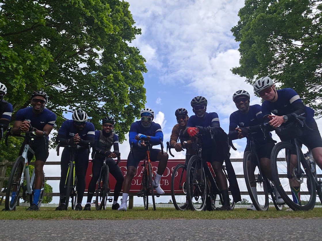 A team of cyclists in matching navy jerseys and helmets posing with their road bikes on a sunny day