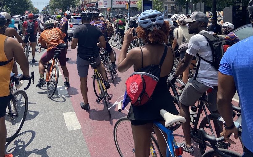 Riders with helmets and backpacks rolling together on a red bike lane in Brooklyn