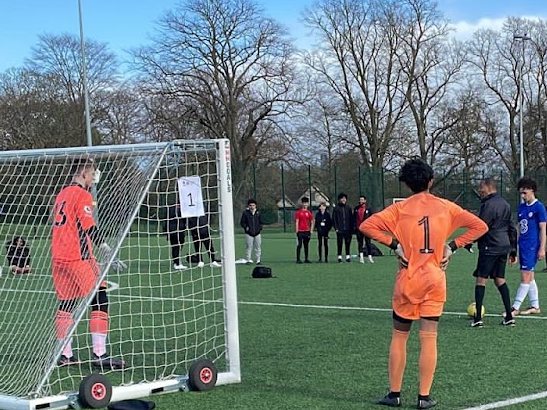Young players in a penalty shootout at a youth football tournament, a goalkeeper in orange waiting by the goal
